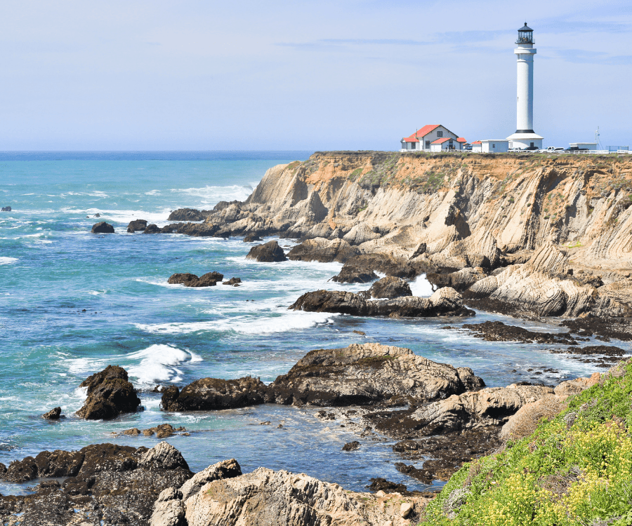 A lighthouse stands on a coastal cliff overlooking the ocean, surrounded by rocky shores and waves.