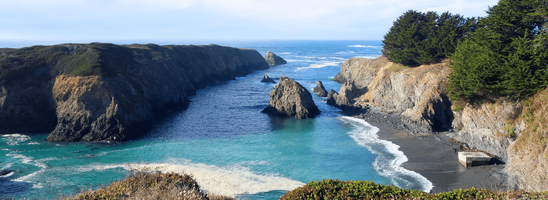 Scenic coastal landscape featuring rocky cliffs, a blue inlet, and lush greenery.