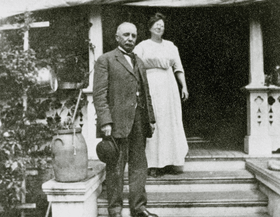 A man in a suit and a woman in a dress stand on the steps of a house.