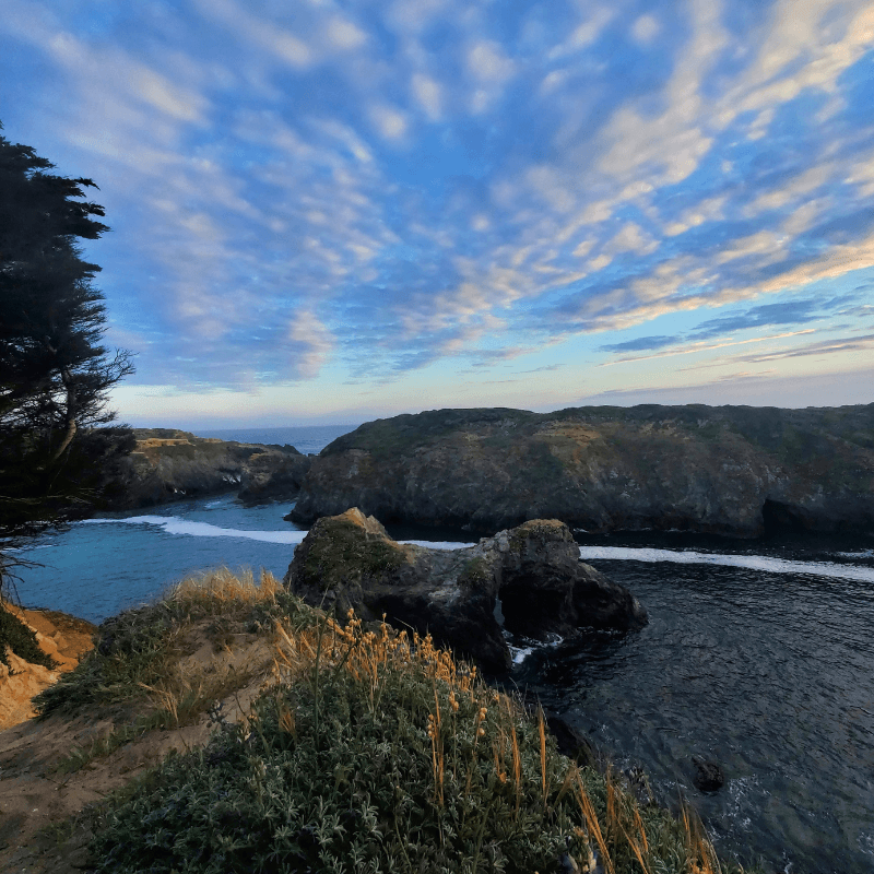 Coastal landscape featuring rocky cliffs, gentle waves, and a dramatic sky filled with clouds.