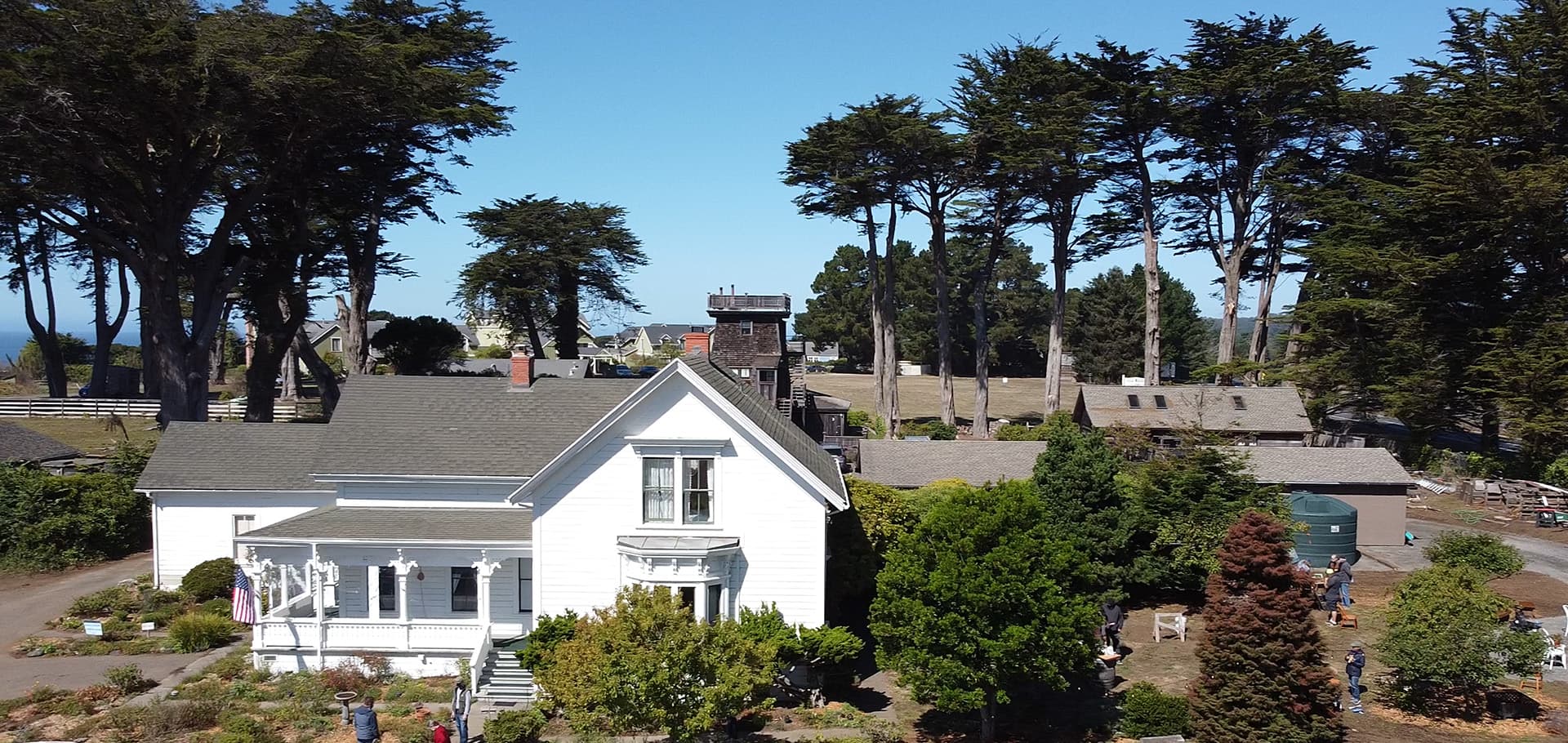 A white house surrounded by trees and people in a scenic outdoor setting.