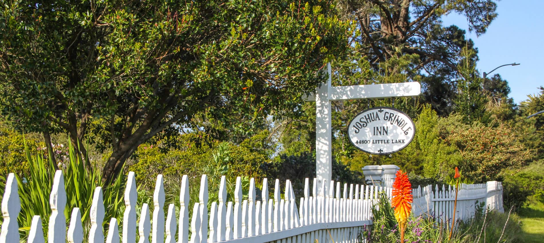 Sign for Joshua Grindle Inn, framed by greenery and a white picket fence.