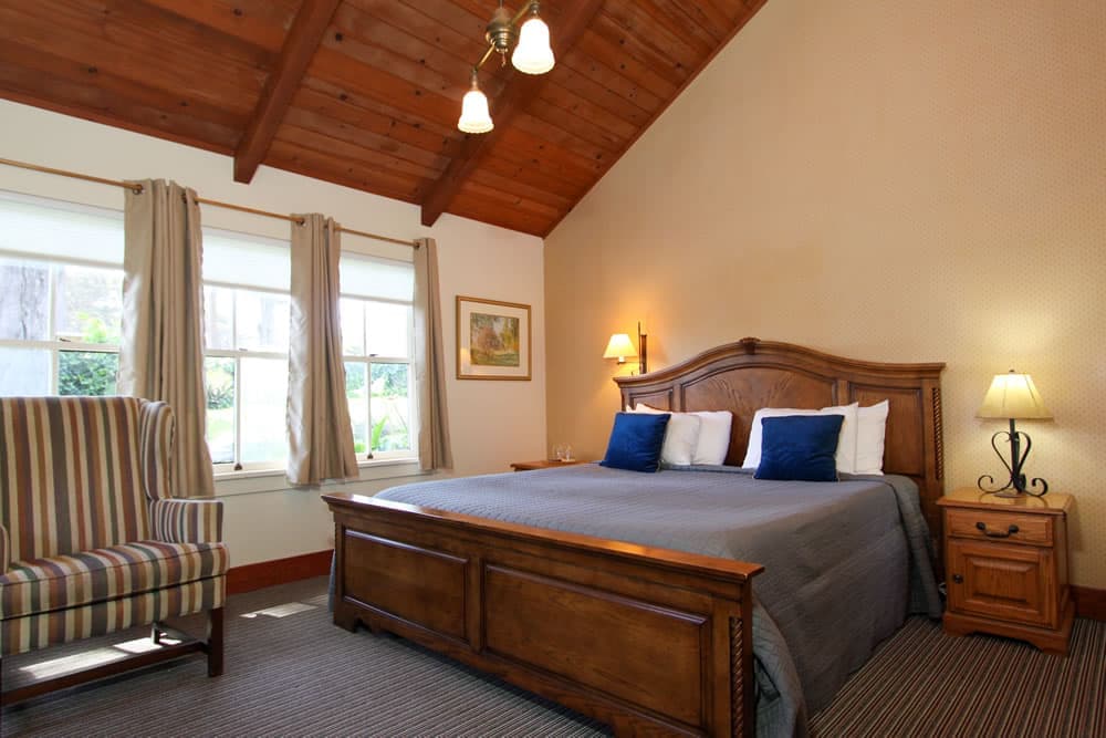 Cozy bedroom with a wooden bed, striped armchair, and large windows.