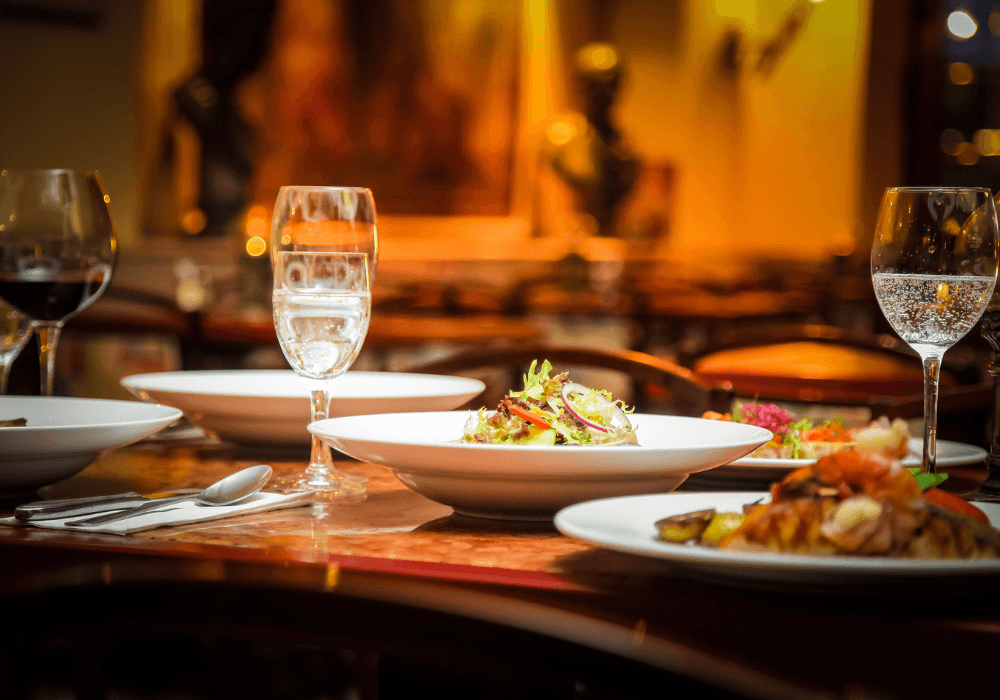 A beautifully set table featuring bowls of food and glasses of water and wine in a warmly lit restaurant atmosphere.