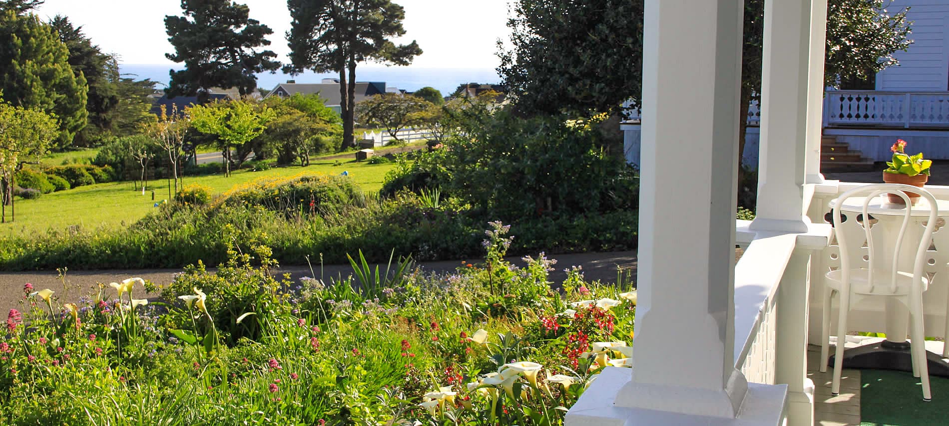 A view of a lush garden and ocean in the distance from a porch.