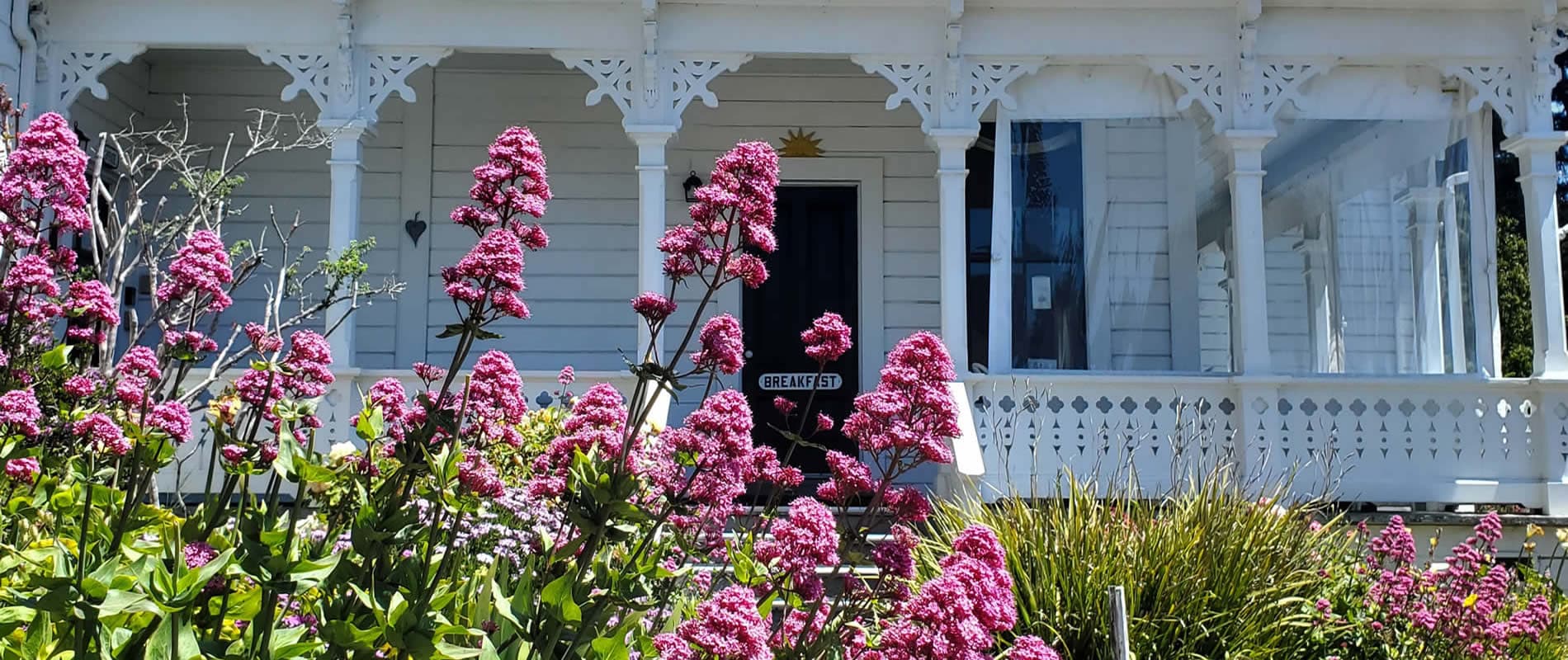 Victorian-style house with a porch, surrounded by vibrant pink flowers.